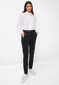 Weißes Hemd mit Knöpfen und Tasche, schwarze maßgeschneiderte Hose und weiße Sneakers. Das Outfit zeichnet sich durch ein einfaches, klassisches Design aus.