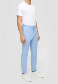 Světle modré kalhoty na míru s hladkou texturou látky, s plochým předním dílem, poutky na opasek a úzkým střihem. Kombinovány s bílými teniskami.