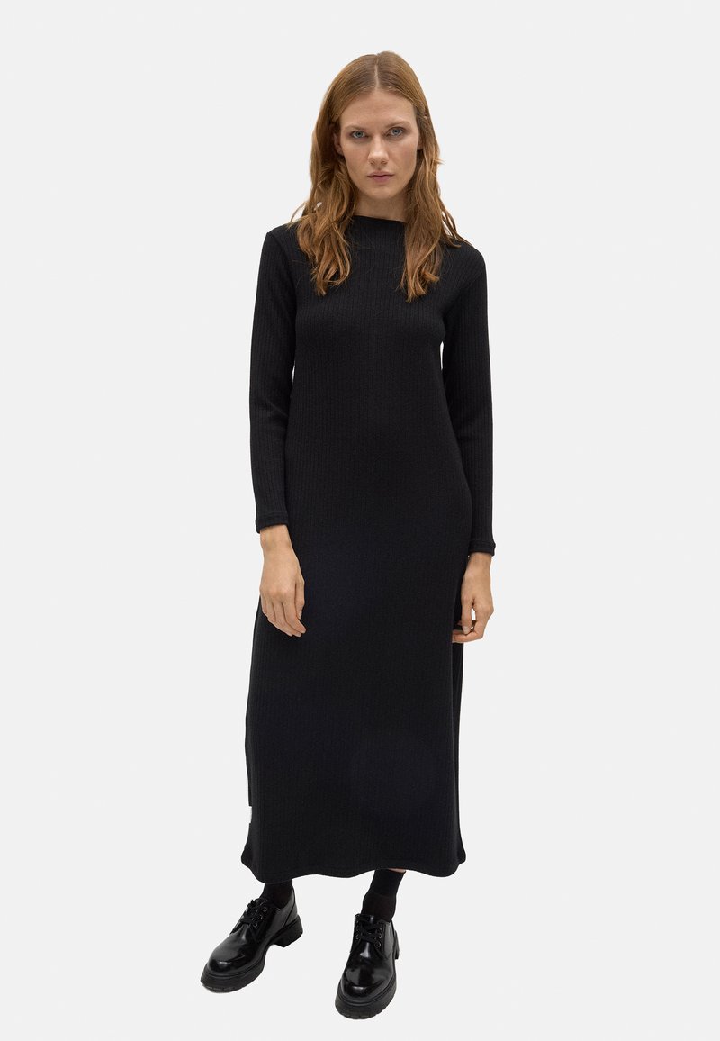 Vestido maxi negro de punto acanalado de manga larga con corte recto, que presenta un escote redondo y una abertura lateral. Llevado con zapatos negros con cordones.