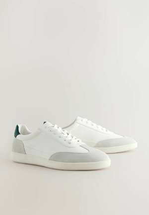 Witte sneakers met een textuur van leer en accenten van suede. Voorzien van een groene hieltab, ronde veters en een rubberen zool. Minimalistisch ontwerp.