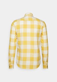Camisa de manga larga a cuadros amarillos y blancos con puños abotonados, mostrada desde la parte posterior sobre un fondo blanco liso.