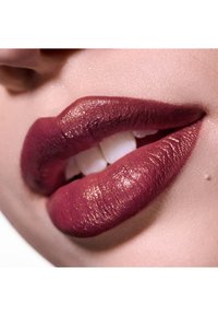 Rouge à lèvres bordeaux profond sur des lèvres lisses et texturées, avec un éclaircissement et une légère brillance. Des dents blanches partiellement visibles entre les lèvres.