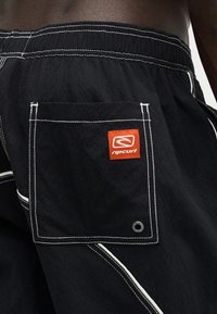 Μαύρο μαγιό με λευκή ραφή, ελαστική μέση, πίσω τσέπη με πορτοκαλί λογότυπο Rip Curl και τρύπα αποστράγγισης.