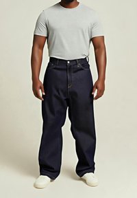Granatowe dżinsowe spodnie o szerokich nogawkach z wysokim stanem, wyposażone w pięć kieszeni i widoczne przeszycia, zestawione z jasnoszarym, krótkim rękawem koszulą.