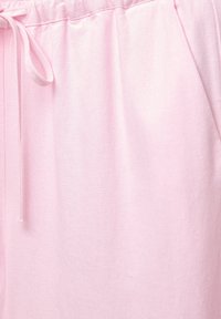 Pantalon en tissu rose clair avec une taille élastique et un cordon noué sur le côté gauche, mettant en valeur les détails de la texture.