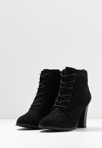 Botines de ante negro con punta afilada, cordones en la parte delantera y un tacón cuadrado alto. Cuenta con una cremallera lateral para facilitar su uso.