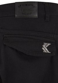 Črne jeanske hlače z usnjenim oznako "KARL KANI" in srebrnim vezenim logotipom na zadnjem žepu. Gladka tekstura, krojena zasnova.