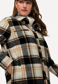 Karierte Jacke in Schwarz-, Weiß- und Beigetönen, mit durchgehender Knopfleiste, Brusttasche und einem kragenförmigen Design aus strukturiertem Stoff.