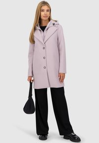 Cappotto lavanda chiaro con cappuccio, caratterizzato da un colletto a punta e bottoni neri. Abbinato a pantaloni neri a gamba larga e una piccola borsa nera.