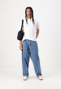 White cotton t-shirt with printed logo, loose light blue denim jeans, and a small black crossbody bag. White sneakers with red accents.