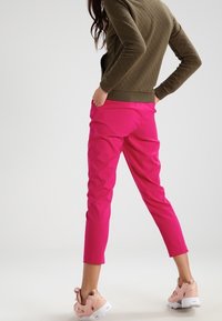 Rosa tights med slim fit och cropped ankle-längd; tillsammans med en olivgrön quiltad sweatshirt och rosa sneakers.