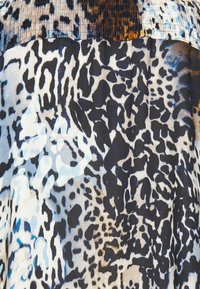 Tryckt tyg med en blandning av svarta, vita och blå leopardfläckar. Materialet är slätt med en glansig textur.