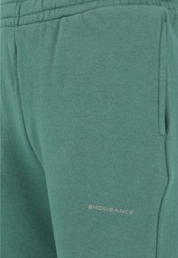 Gröna sweatpants i mjukt material, med elastisk midja, sidofickor och en silverfärgad "ENDURANCE"-logotyp på låret.