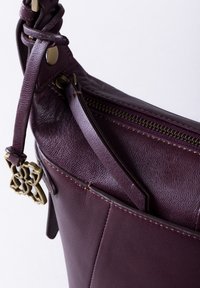 Burgundy leather bag with a textured finish, featuring a zippered closure, adjustable strap, and a decorative metal accent.