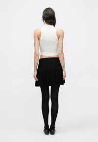 Biely krátky top bez rukávov, čierna rozšírená sukňa, čierne pančuchy a čierne baleríny. Hladké textúry, priliehavý dizajn a minimalistický štýl.