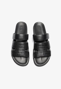 Svarte skinnsandaler med teksturert krokodillemønster og brede stropper. Glatt, flat såle med preget logo på oversiden.