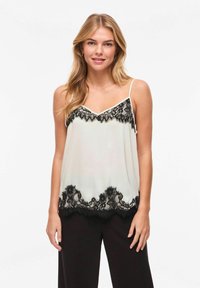 Camisole en satin ivoire ornée de dentelle. Encolure en V avec accents de dentelle noire le long de la poitrine et de l'ourlet. Bretelles spaghetti ajustables.