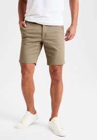 Pantaloni corti khaki realizzati in tessuto misto cotone, con vita piana, tasche laterali e una vestibilità comoda, abbinati a sneaker bianche.