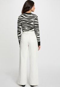 Un haut à rayures noires et blanches à manches longues associé à un pantalon blanc à taille haute et à jambes larges. La texture est lisse, et le pantalon possède des poches arrière.