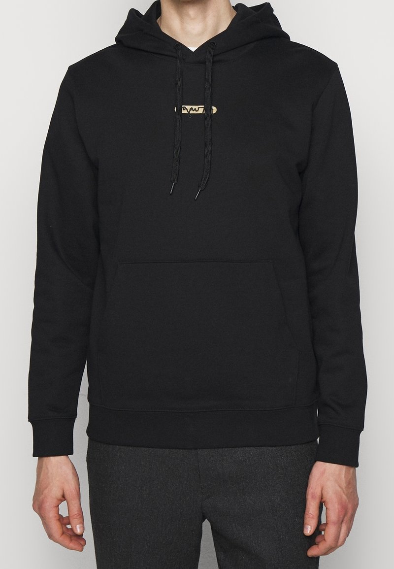 Sudadera negra con capucha en tela suave con un bolsillo tipo canguro, que presenta un emblema dorado en el pecho y cordones ajustables.