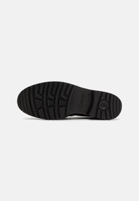 Suela de zapato de goma negra con un patrón de relieve texturizado y un pequeño acento circular. El logo "Gabor" está grabado cerca del centro.