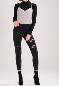 Jeans skinny neri strappati, top grigio a spalla sottile indossato sopra un dolcevita nero a costine. Indossato con stivali neri con tacco alto alla caviglia.