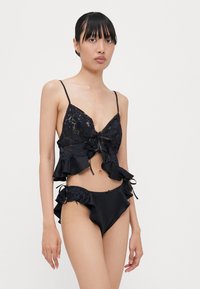 Melnas mežģīnes un satīna bikinis, kurā ir īss tops ar volānu apmalīti un regulējami savilcēji, papildināts ar volānu bikini apakšdaļu.