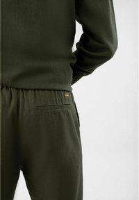 Groene, gestructureerde stoffen outfit met een relaxte pasvorm top en elastische taillebroek, met een klein oranje logo en een enkele achterzak.