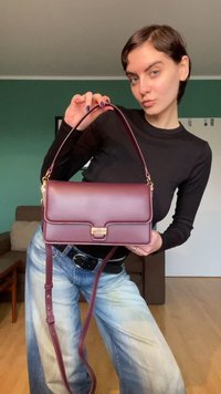 Bordeauxkleurige handtas van kunstleer met een rechthoekige vorm, gouden beslag, een platte voorflap en een verstelbare schouderriem.