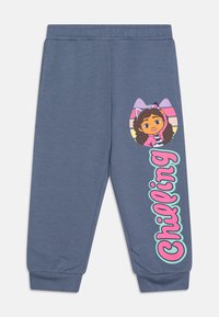 Zilā sporta bikses ar ribotām apakšmalām, ar raksturu grafiku un tekstu "Chilling" rozā un miņu akcentos kreisajā kājā.