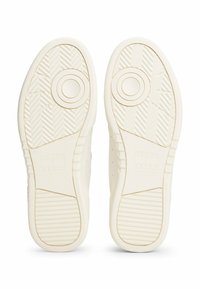 Suelas de zapatillas blancas con patrones de agarre texturizado y acentos circulares. Marca visible en la parte inferior. Material suave y duradero.