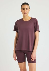 Maglietta sportiva a maniche corte color bordeaux con collo tondo, abbinata a pantaloni corti bordeaux coordinati. Entrambi i capi sono realizzati in tessuto morbido e elastico.