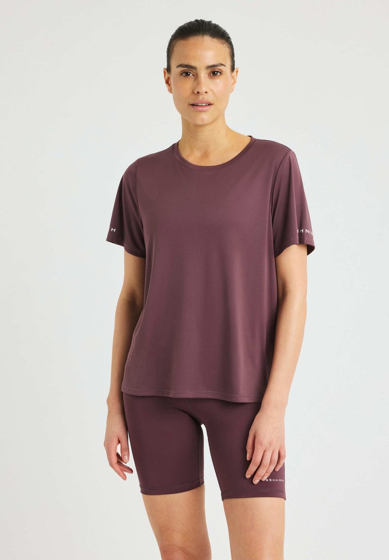 Maglietta sportiva a maniche corte color bordeaux con collo tondo, abbinata a pantaloni corti bordeaux coordinati. Entrambi i capi sono realizzati in tessuto morbido e elastico.