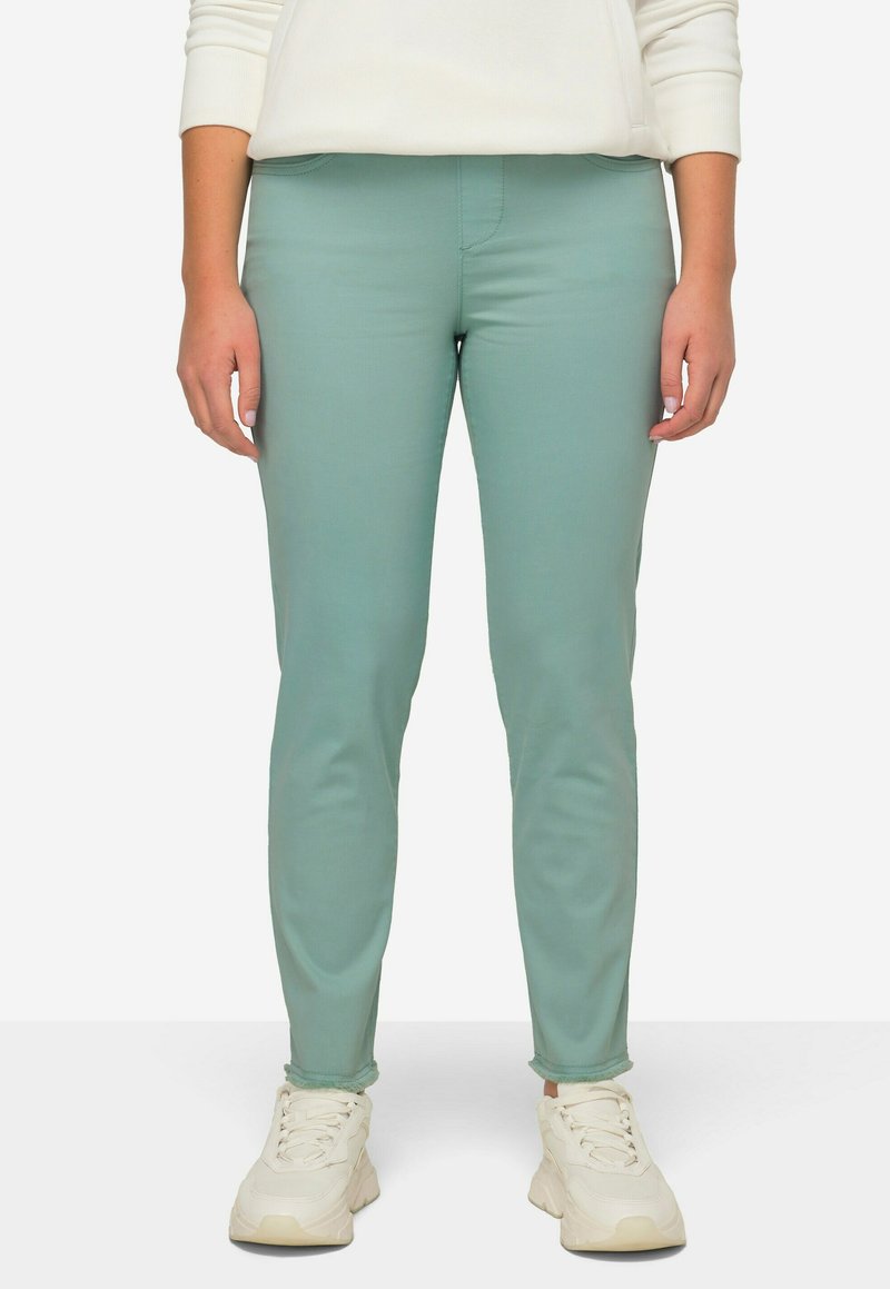 Pantalones ajustados verde menta con una textura suave, con una cintura de altura media y detalles de costura estándar, combinados con zapatillas blancas.