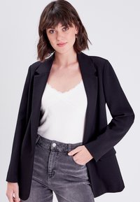 Black blazer with a tailored design, featuring a single-button closure, notched lapels, and two front pockets, worn over a white lace-trimmed top.
