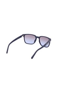 Gafas de sol negras mate con lentes degradados, forma rectangular y acentos metálicos. Logotipo brillante "GANT" en el lado exterior de la patilla.