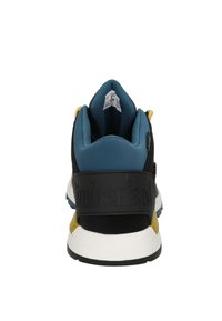 Zapatilla negra y azul con una superficie texturizada, cuello acolchado, acentos amarillos y un pronunciado logo de "Timberland" en la correa trasera.