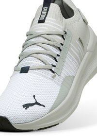 Weißer Sportschuh mit einem strukturierten Mesh-Obermaterial, grauen Akzenten und einer Gummisohle. Verfügt über ein Schnürdesign und ein Puma-Logo an der Seite.