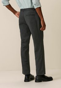 Pantalons ajustés gris foncé avec une coupe slim, dotés d'une poche arrière simple et associés à des chaussures de ville noires. Texture de tissu lisse.