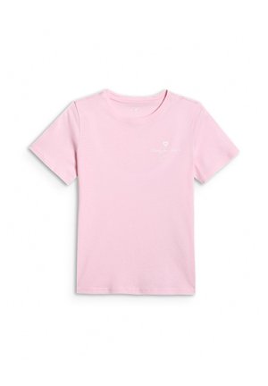Młoda dziewczyna w różowym t-shircie i czapce, granatowych spodniach oraz czarno-białych trampkach, stojąca na szarym tle.