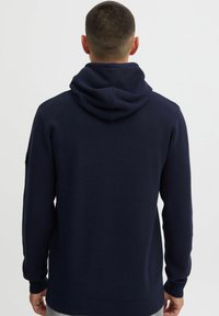 Haut à capuche bleu marine avec une texture douce, une poche kangourou, une capuche réglable avec cordon et des poignets et un ourlet côtelés.
