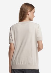 Ljusbeige kortärmad tröja med rund halsringning, ribbade muddar och fåll, och en slät struktur, visad bakifrån.