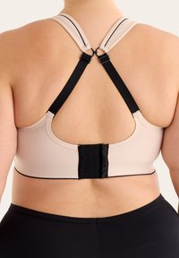 Beige sportbehå med racerback-design och svarta remmar. Har en krok-och-öga-stängning bak och kontrasterande kant.