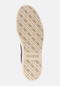 Scarpa nera con texture e suola beige decorata da un motivo. Presenta un design logo ripetuto e il marchio "GUESS" sul lato della suola.
