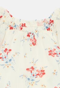Lett, kremfarget stoff med et blomstermønster i rødt, rosa og blått. Rynket halsutskjæring og delikate elastiske trimdetaljer.
