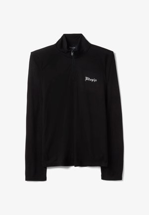 Chemise noire à manches longues avec fermeture éclair quart de zip et texte blanc « Utopia » sur la poitrine gauche, taille moyenne, fond uni.