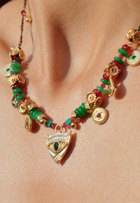 Collier doré avec des perles vertes, rouges et turquoise ; comprend un pendentif triangulaire avec un motif d'œil et des accents décoratifs.