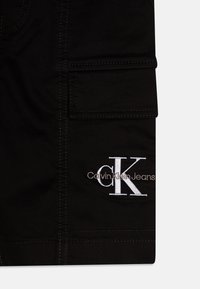 Crne cargo kratke hlače izrađene od pamuka s glatkom teksturom. Sadrže zakrhni džep i izvezenu "CK" oznaku s natpisom "Calvin Klein Jeans".