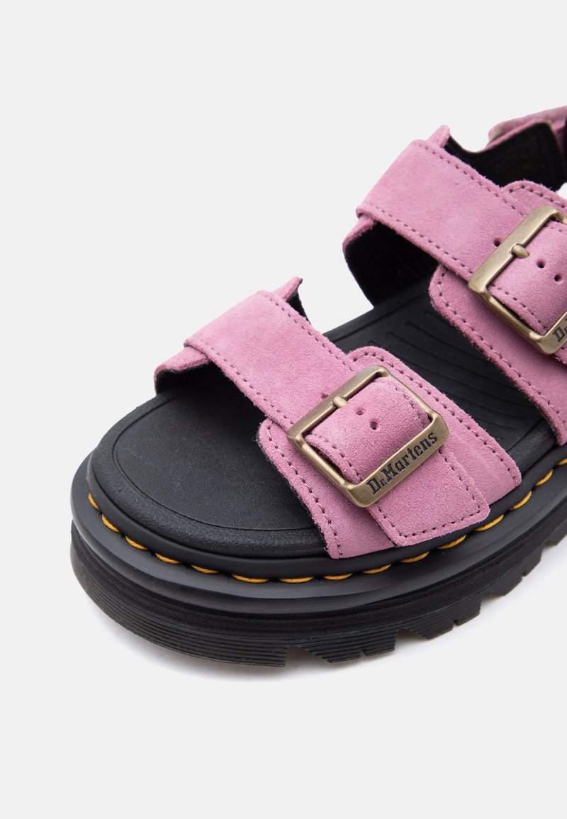 Klobiger Sandalen mit schwarzer Sohle, pinken Velourslederriemen und Messing-Schnallen, detaillierten gelben Nähten und "Dr. Martens"-Markierung auf den Schnallen.