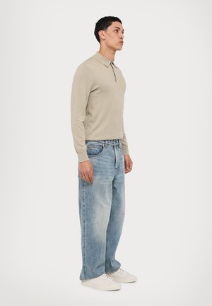Helle beige Langarm-Polo mit Kragen, kombiniert mit hellblauen, locker sitzenden Jeans und weißen Sneakers, im lässigen Design.